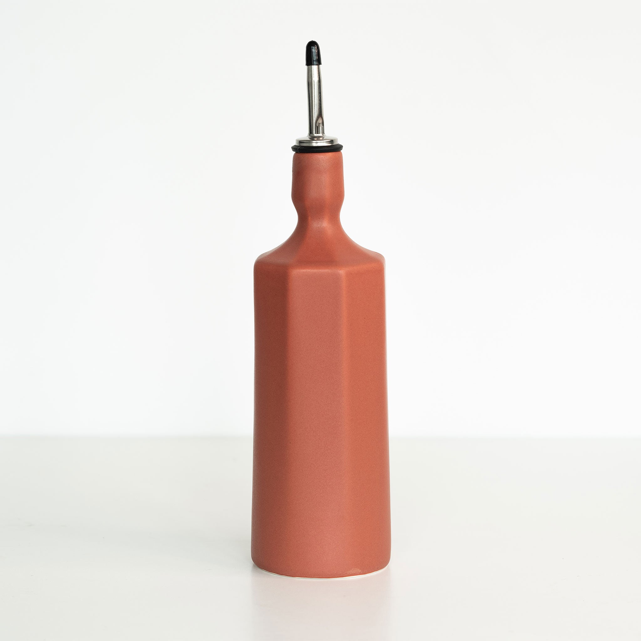 Terracotta-colored oil bottle with a black cap on a white background