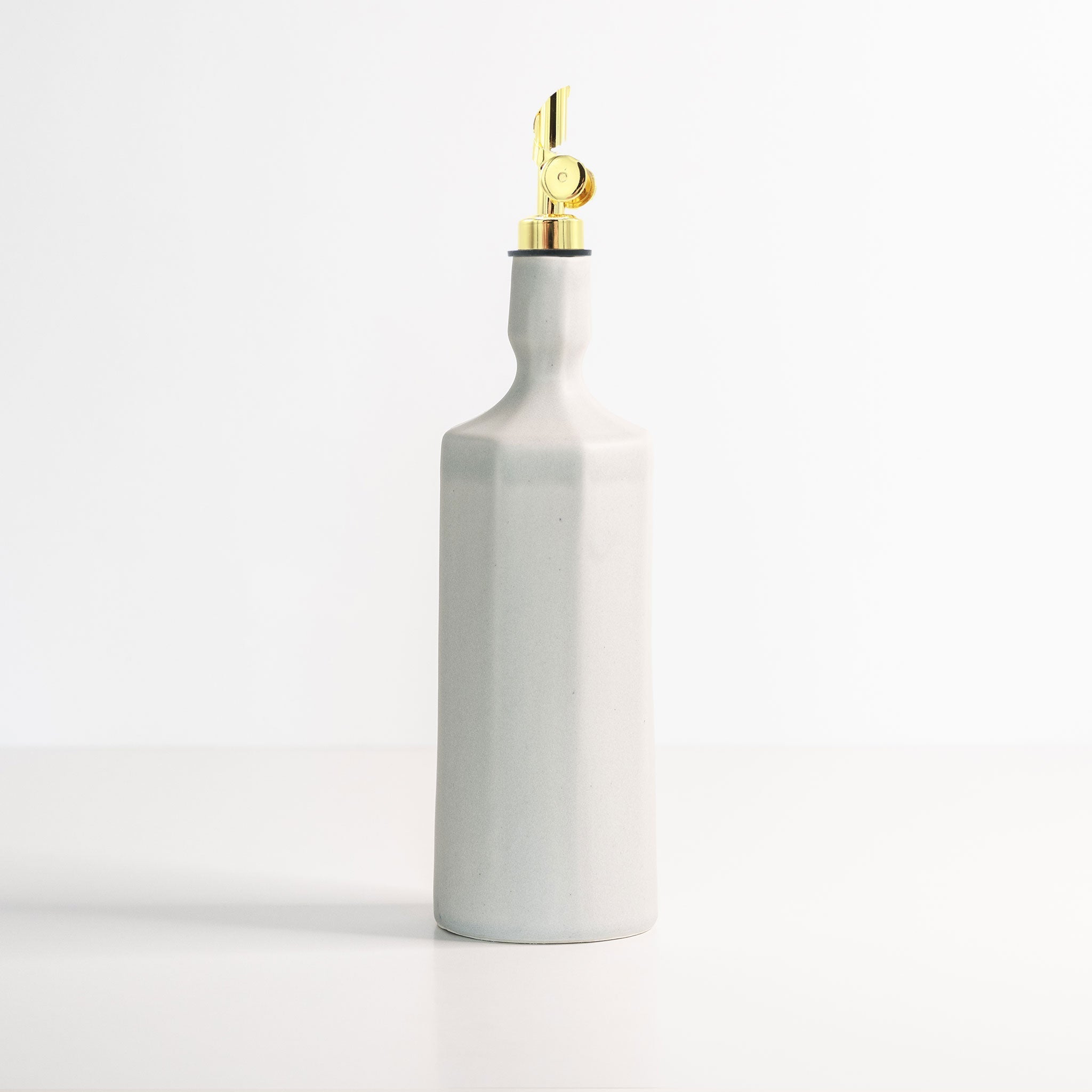 White ceramic oil bottle with gold cap on a white background