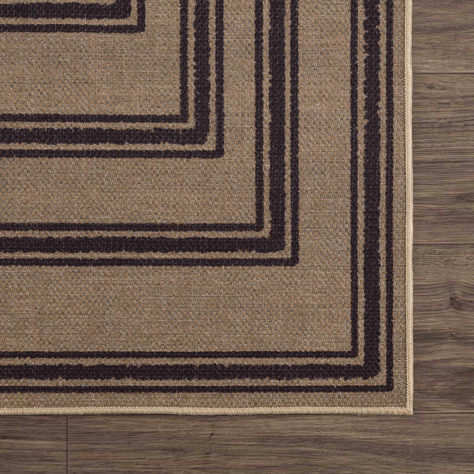 Close-up of a brown rug with black geometric patterns on a wooden floor.