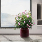 Floral arrangement in a red pot on a wooden floor with a large window in the background