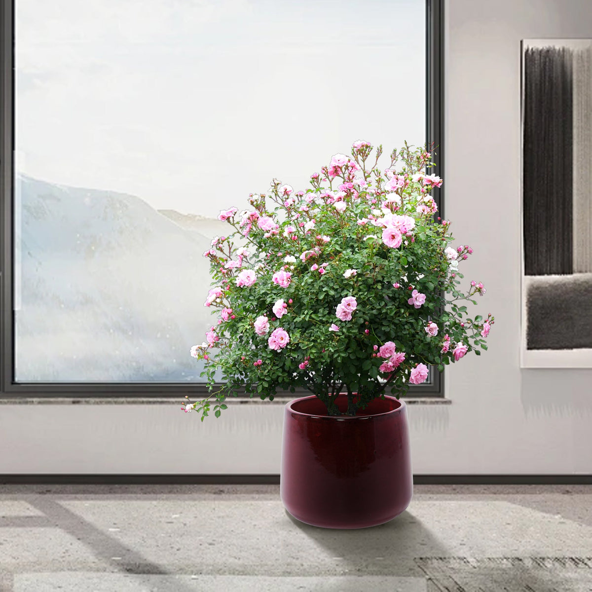 Floral arrangement in a red pot on a wooden floor with a large window in the background