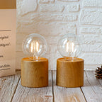 Two wooden table lamps with clear glass bulbs on a light wooden surface.