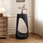 Modern black side table with a vase of flowers in a room with wooden flooring and a lamp.