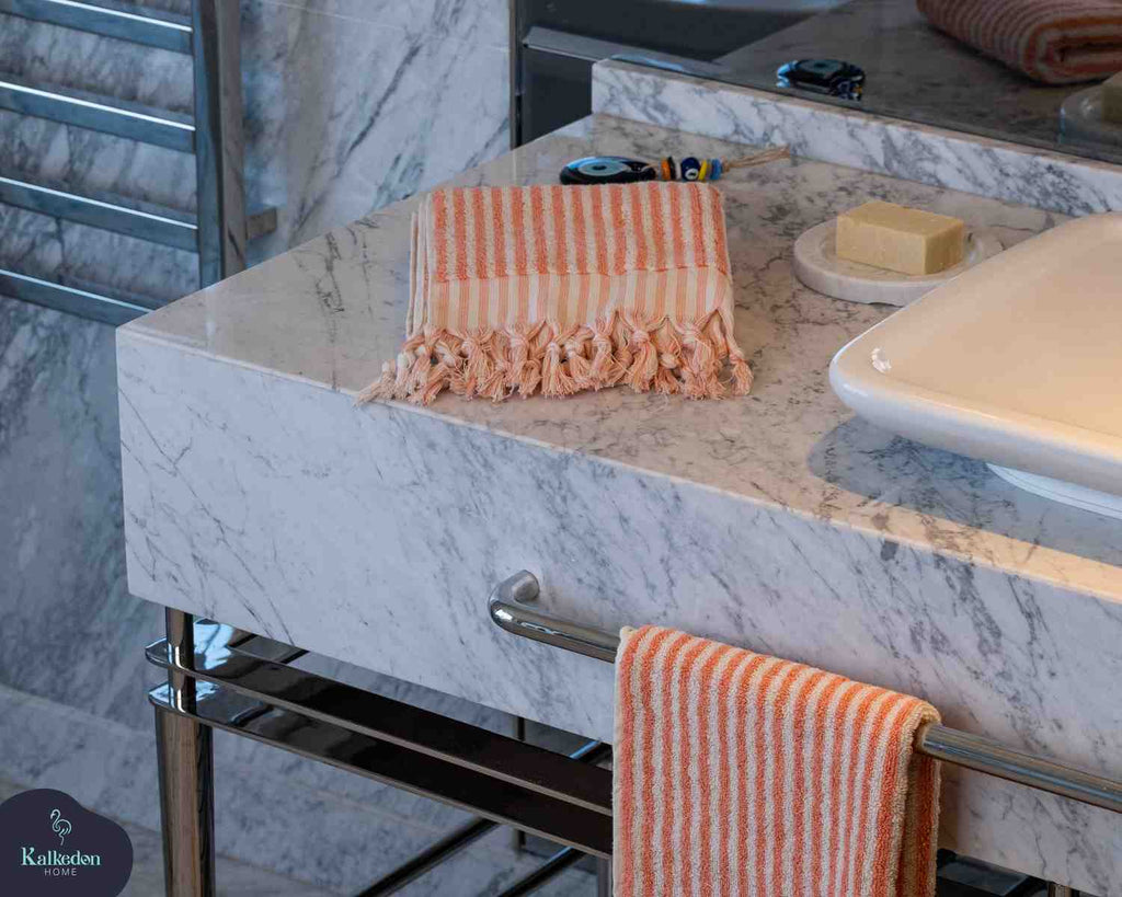 Striped orange and white hand towel with fringe on marble bathroom counter