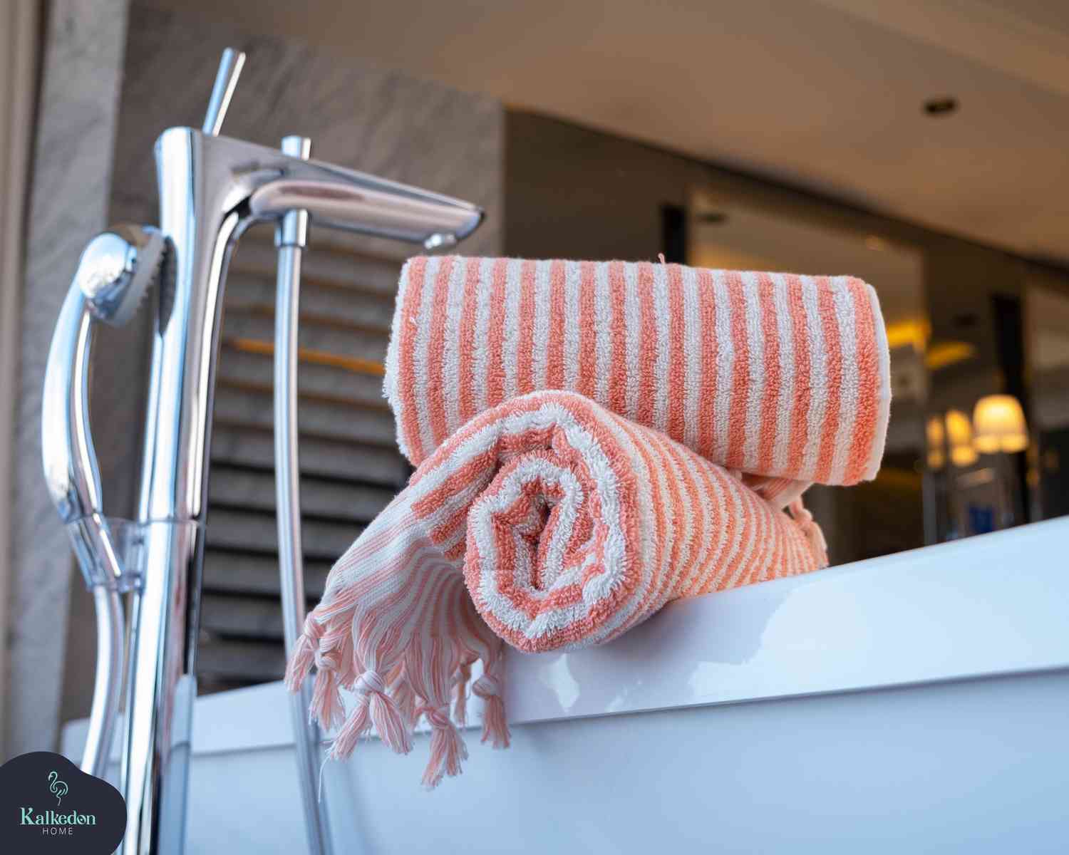 Folded pink and white striped hand towel with tassels on a bathtub edge