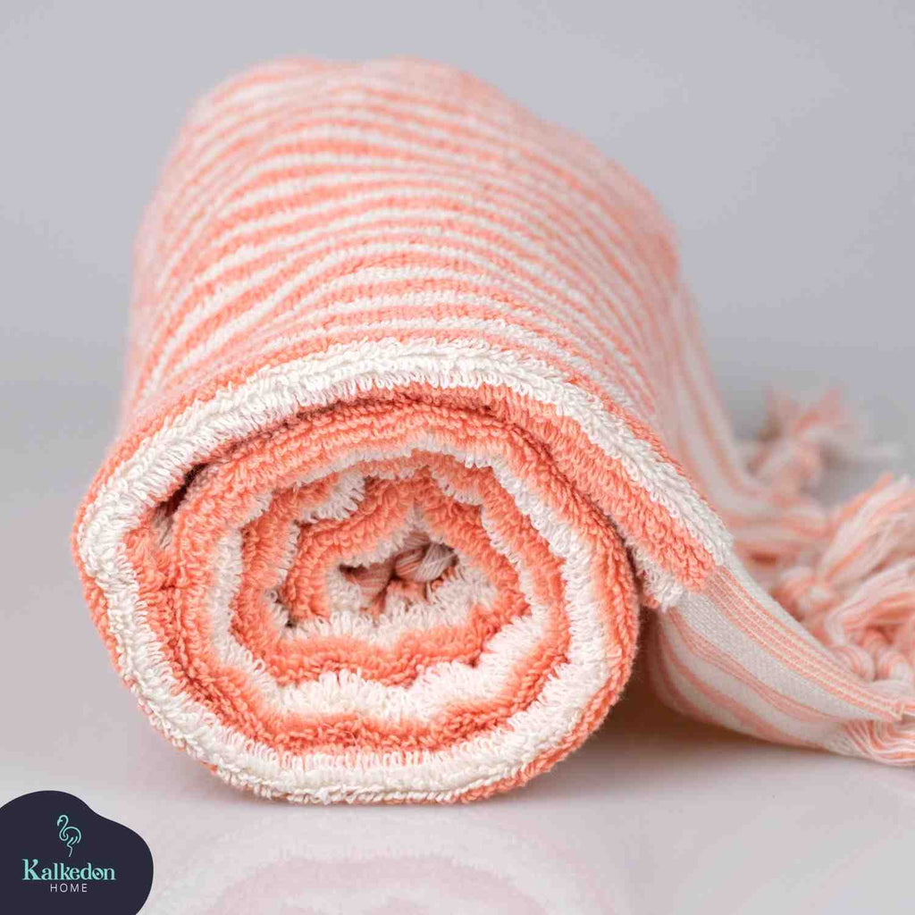 Folded pink and white striped hand towel with tassel edges, rolled on a plain surface.