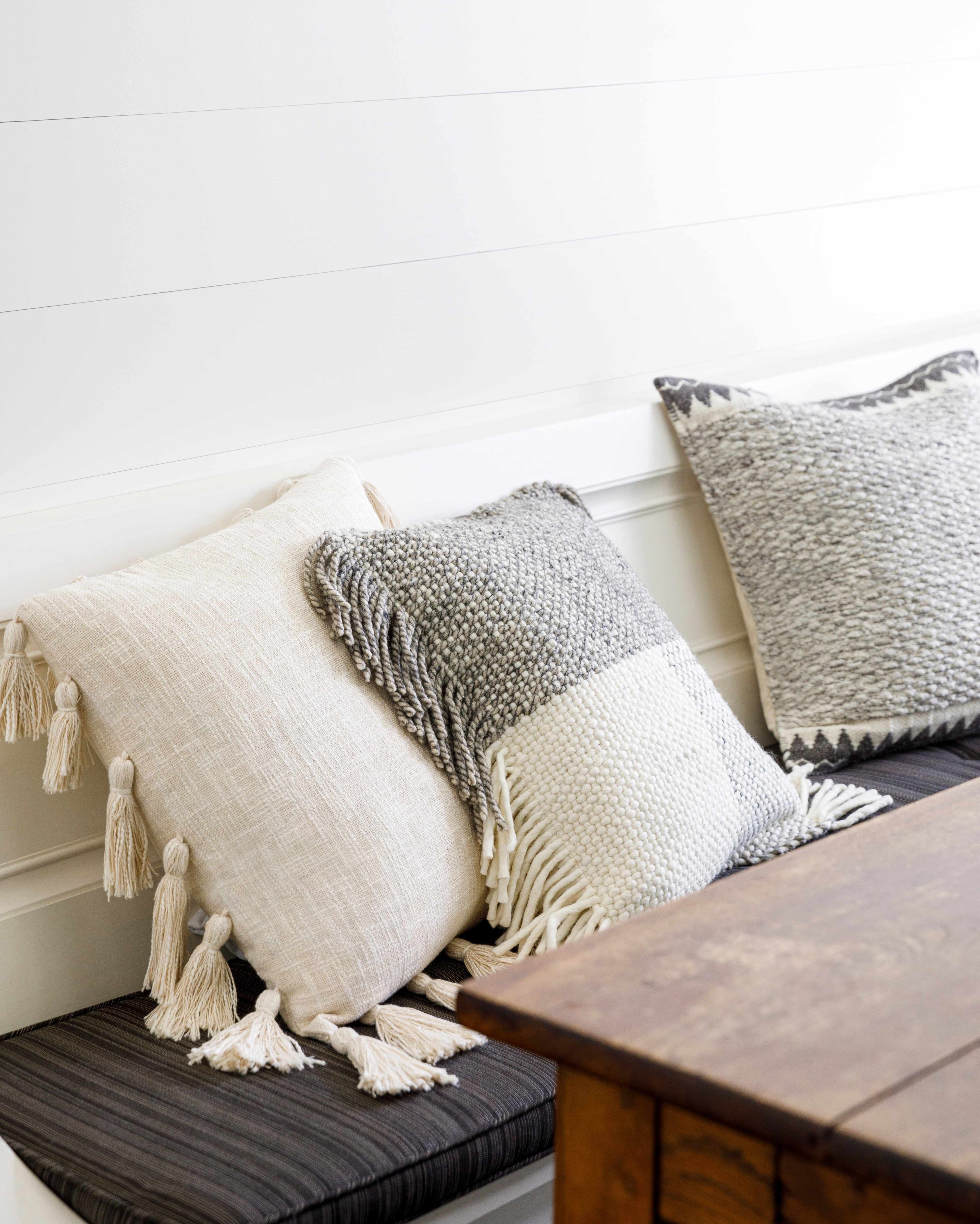 Decorative pillows with tassels on a wooden bench against a white wall.