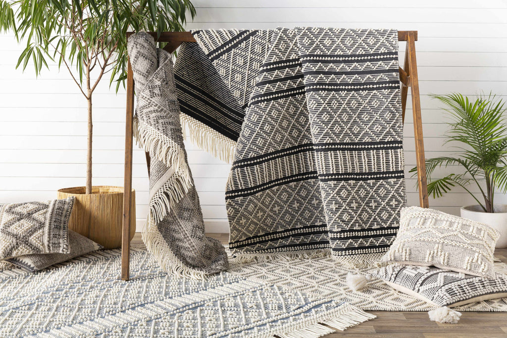 Black and white patterned throw blanket on a wooden rack with plants and pillows in the background.
