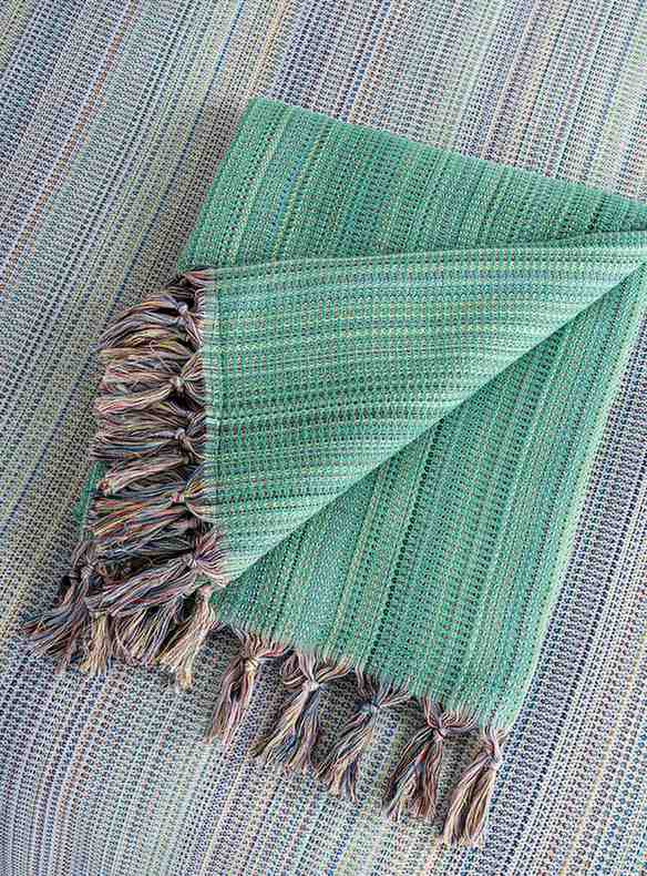 Folded green king size blanket with fringe, textured weave, laid on matching surface