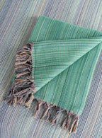 Folded green king size blanket with fringe, textured weave, laid on matching surface