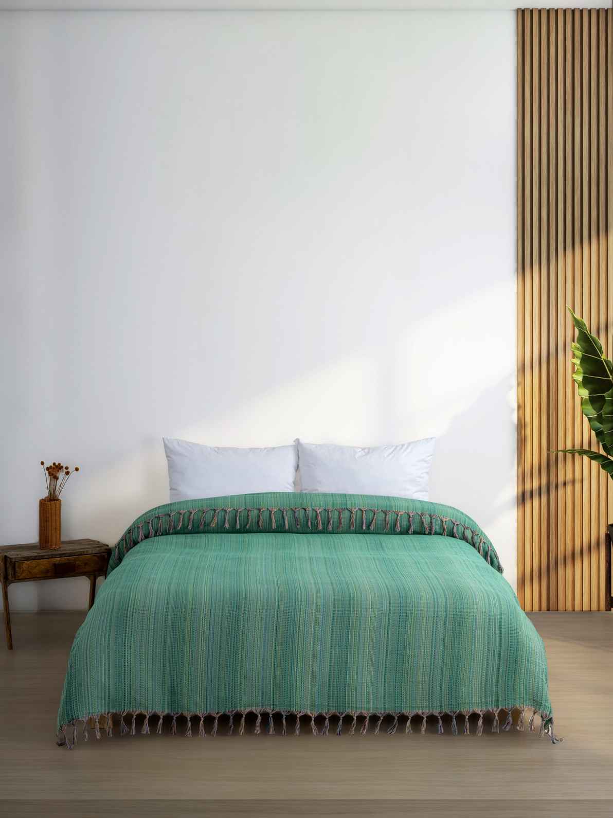 Green king size blanket with tassels on a neatly made bed in a modern minimalist bedroom