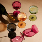 Colorful cocktail glasses on a beige surface with a bottle of wine.