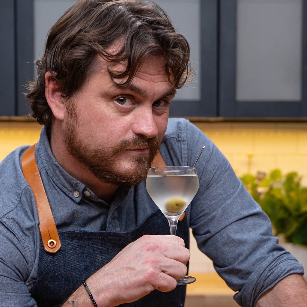 Man holding a glass of cocktail in a kitchen setting