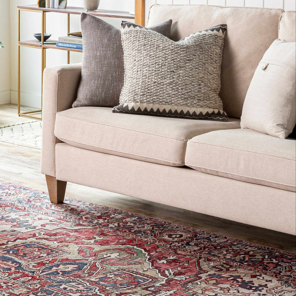 Beige sofa with patterned cushions on a decorative rug in a living room setting.