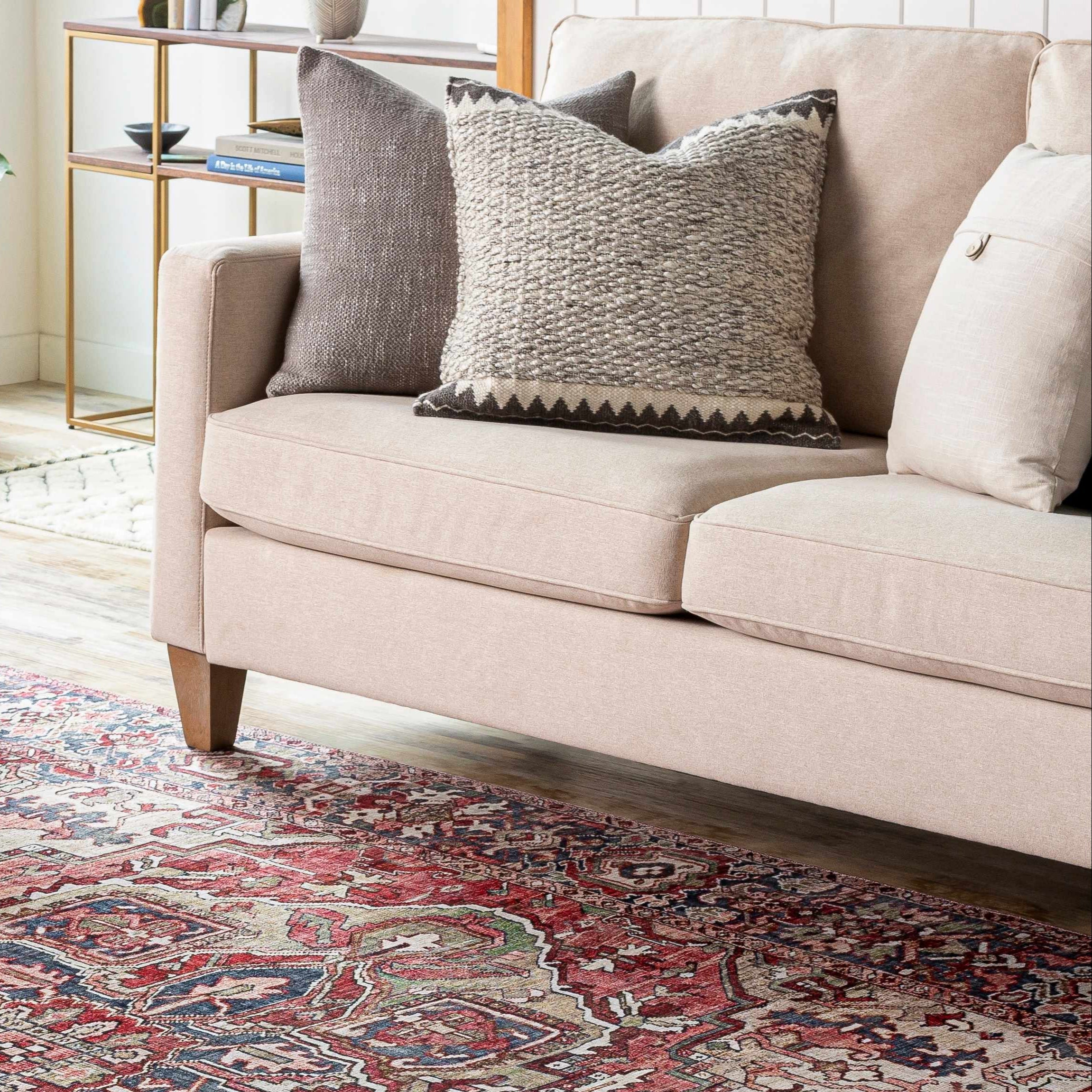 Beige sofa with patterned cushions on a decorative rug in a living room setting.