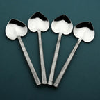 Four silver spoons with unique designs on a dark green background