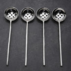 Four metal ladles with perforated ends on a dark gray background