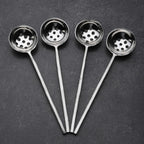 Set of four metal ladles with perforated bowls on a dark surface