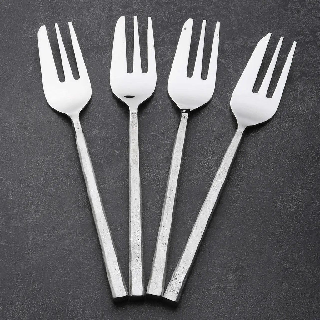 Four silver metal serving forks with long, textured handles arranged in a fan shape on a dark gray textured background.