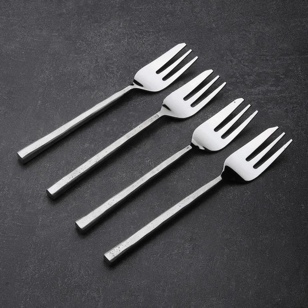 Set of four silver dessert forks on a dark surface