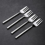 Set of four silver dessert forks on a dark surface