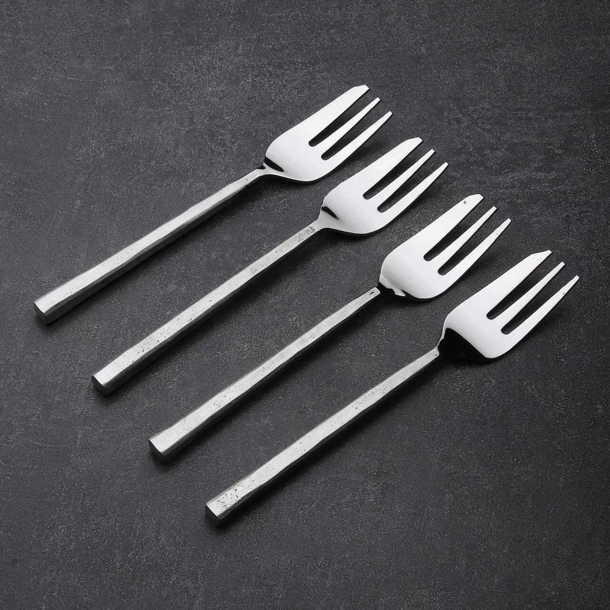 Set of four silver dessert forks on a dark surface