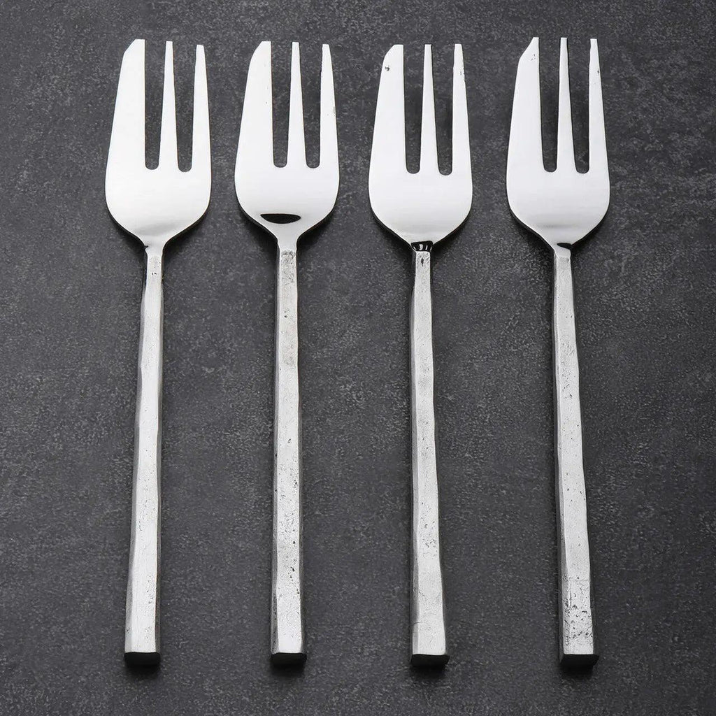 Four silver pastry forks on a dark gray background