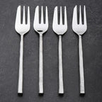 Four silver pastry forks on a dark gray background
