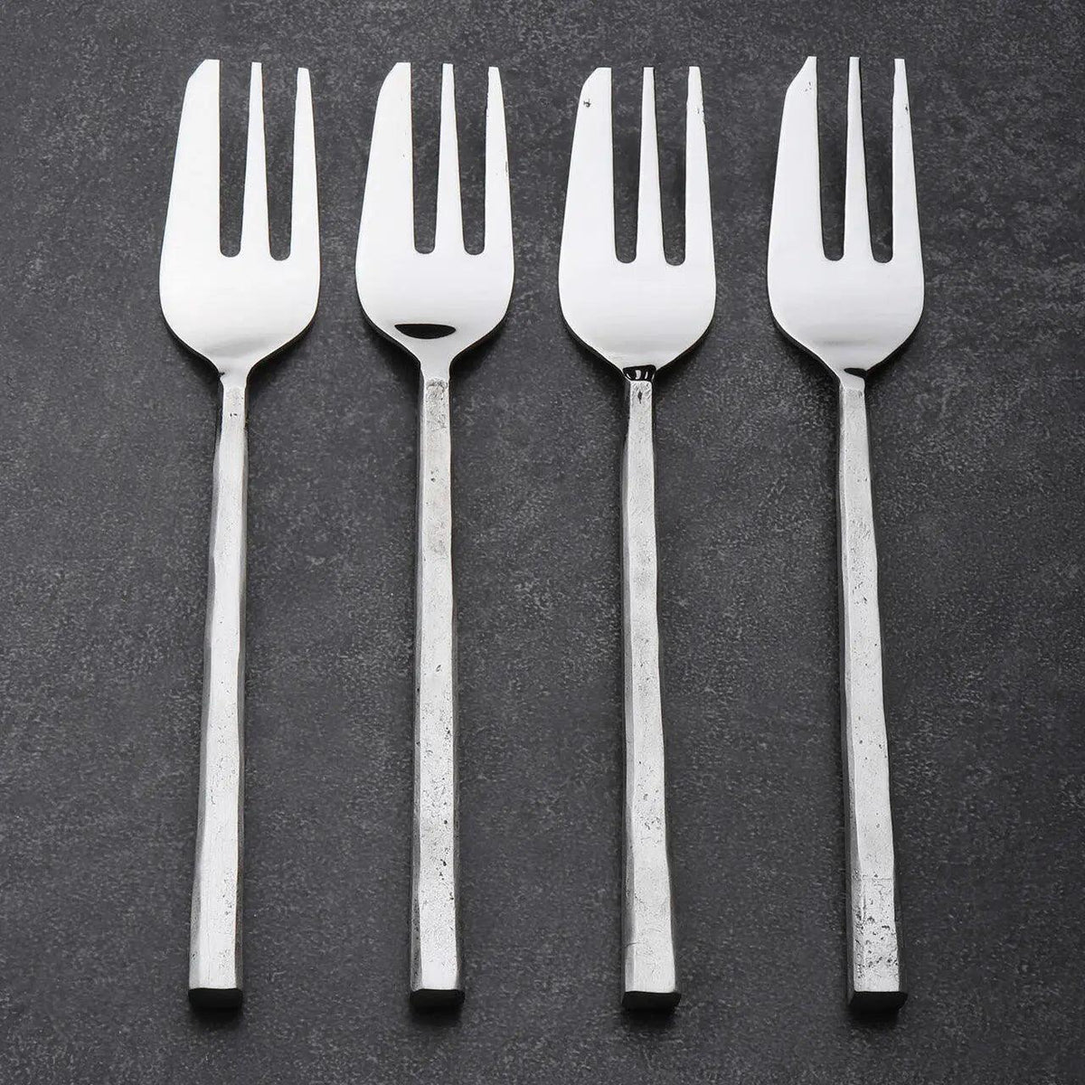 Four silver pastry forks on a dark gray background