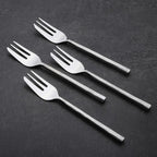 Four silver pastry forks on a dark gray background