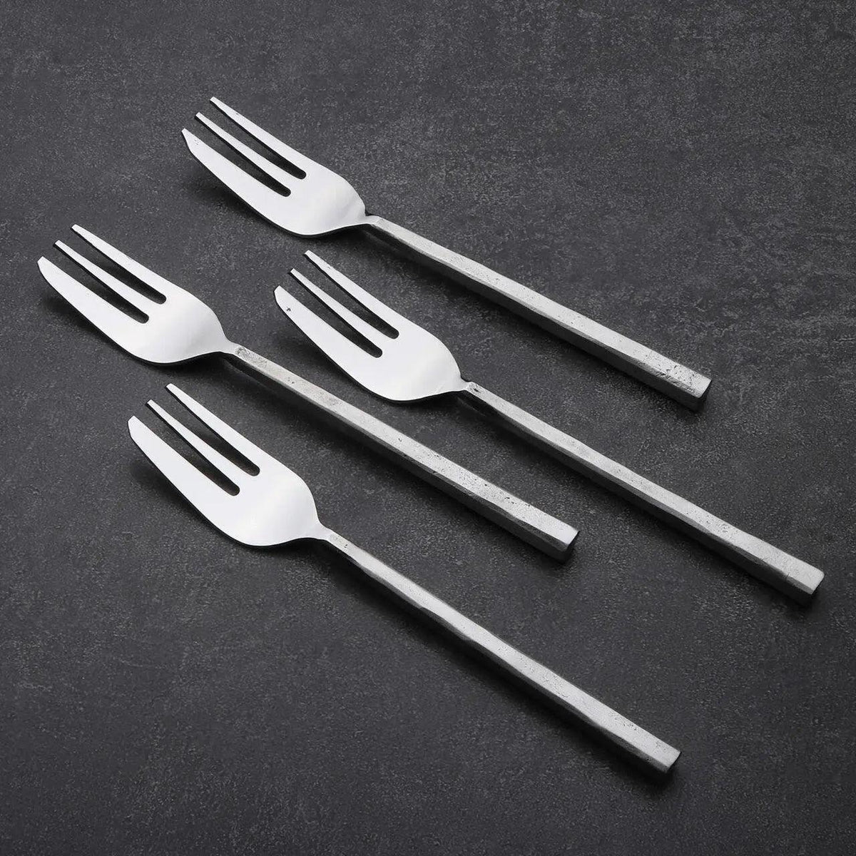 Four silver pastry forks on a dark gray background