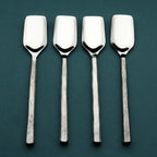 Set of four silver stilton spoons on a dark green background
