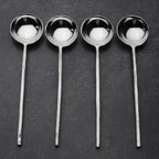Set of four steel sugar spoons on a dark surface