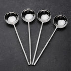 Set of four steel sugar spoons on a dark surface