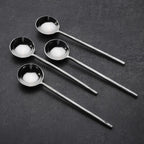 Set of four steel sugar spoons on a dark surface