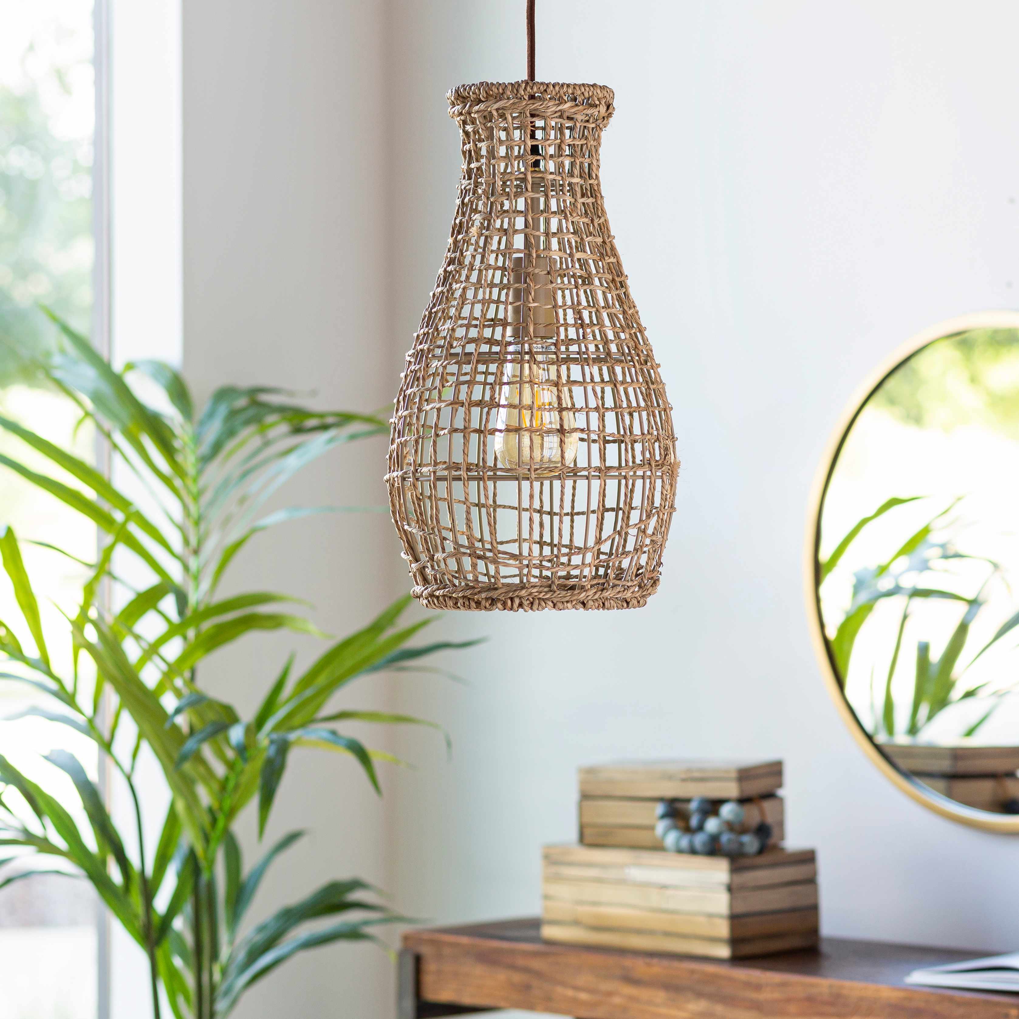 Woven pendant light hanging in a room with a plant and books on a table.