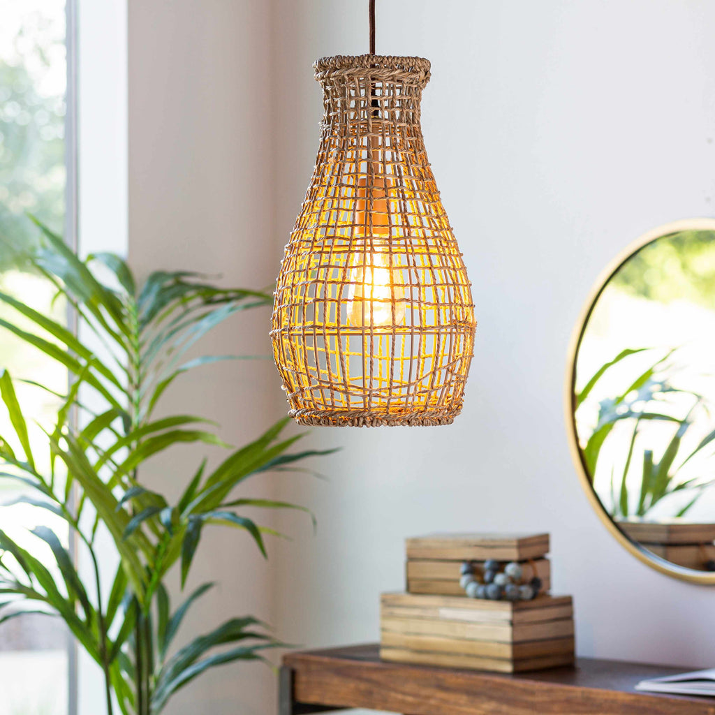 Woven pendant light hanging in a room with a plant and books on a table.