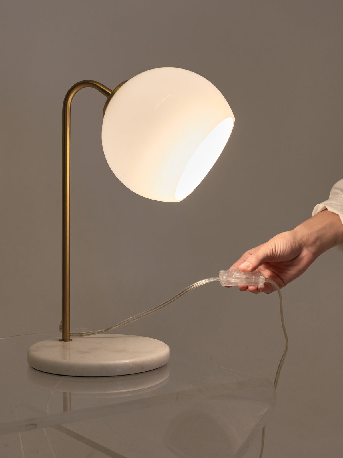 Table lamp with marble base and gold arm, being unplugged by a hand on a reflective surface.
