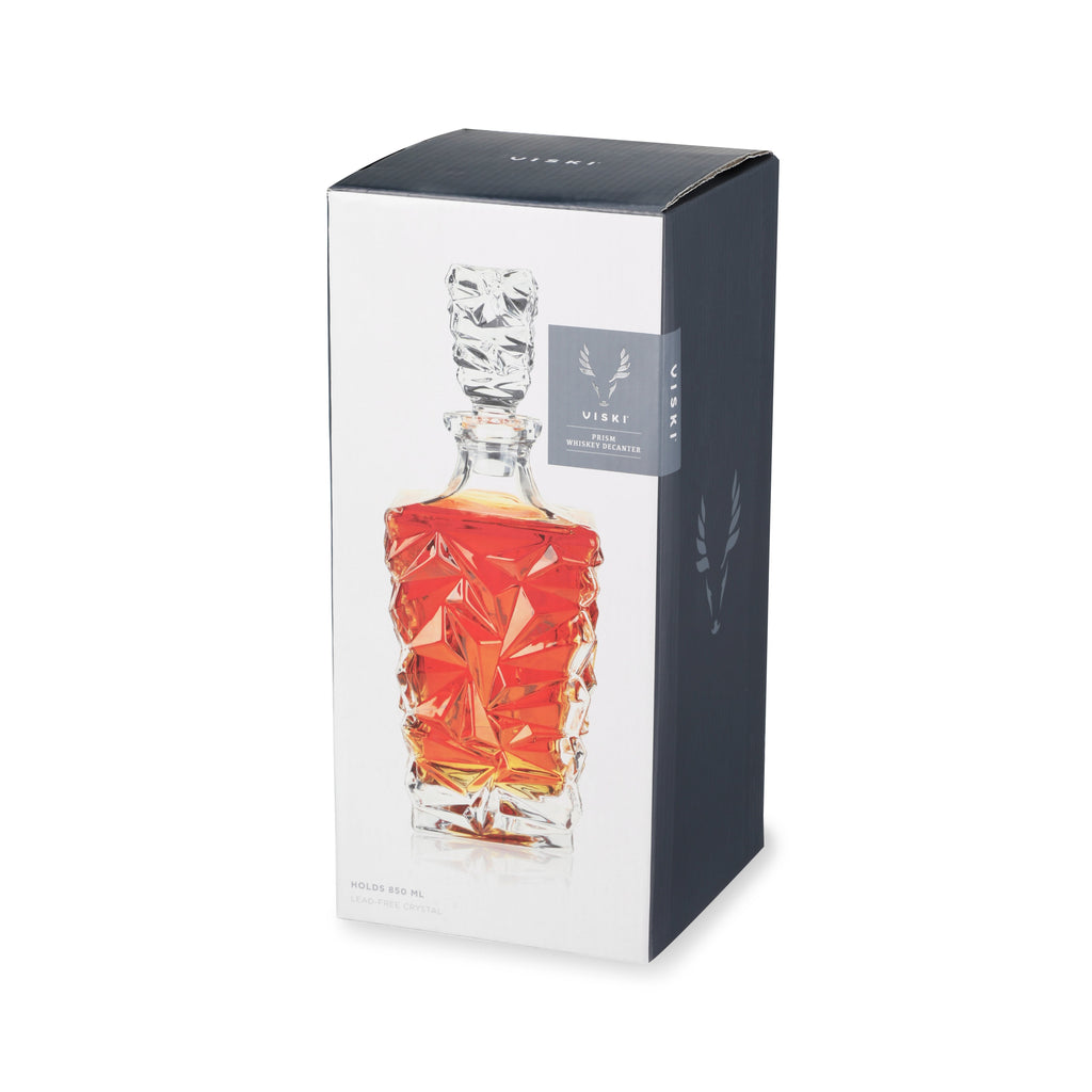 Crystal decanter with amber liquid in a branded box on a white background