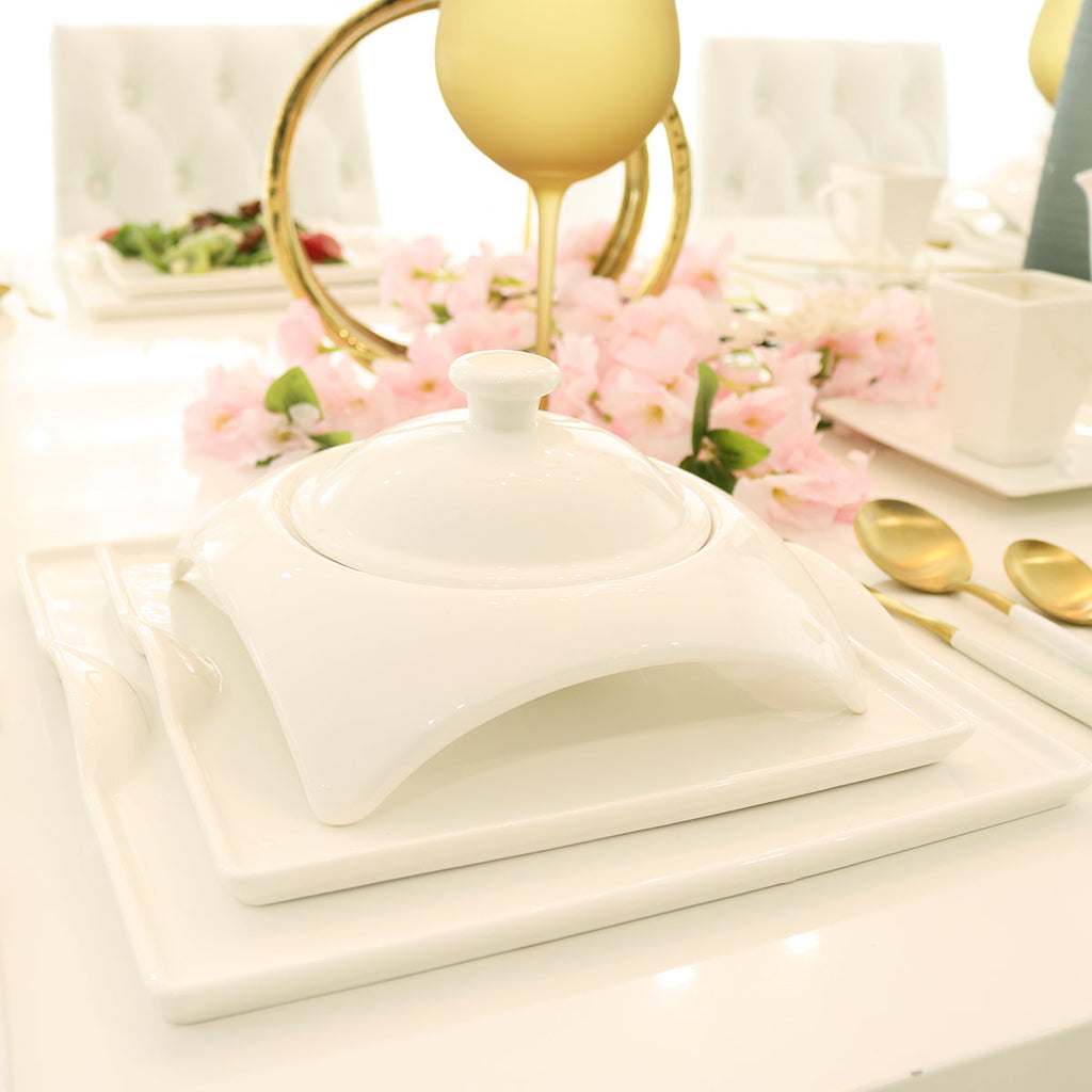 Elegant white ceramic serving dish on modern dining table with gold cutlery and pink flowers