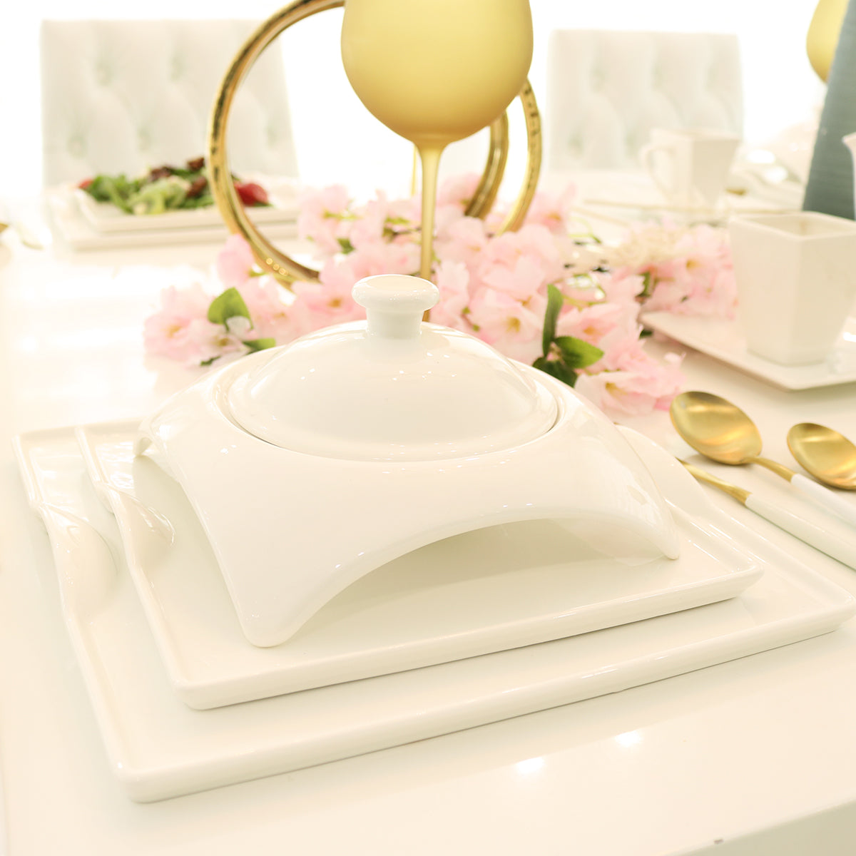 Elegant white ceramic serving dish on modern dining table with gold cutlery and pink flowers