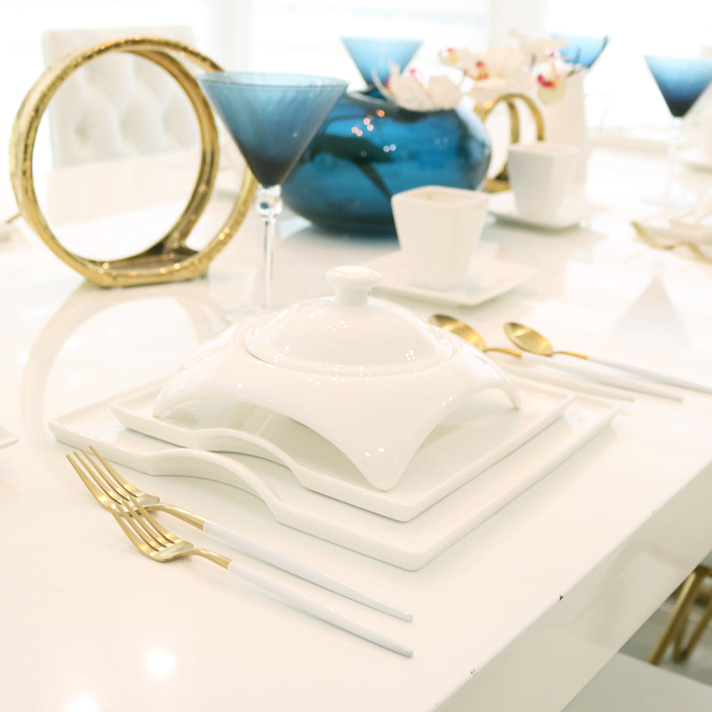 Elegant modern table setting with white dinnerware, gold cutlery, blue glassware, and centerpiece