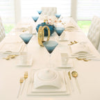 Elegant modern dining table with blue martini glasses, gold cutlery, and white dinnerware