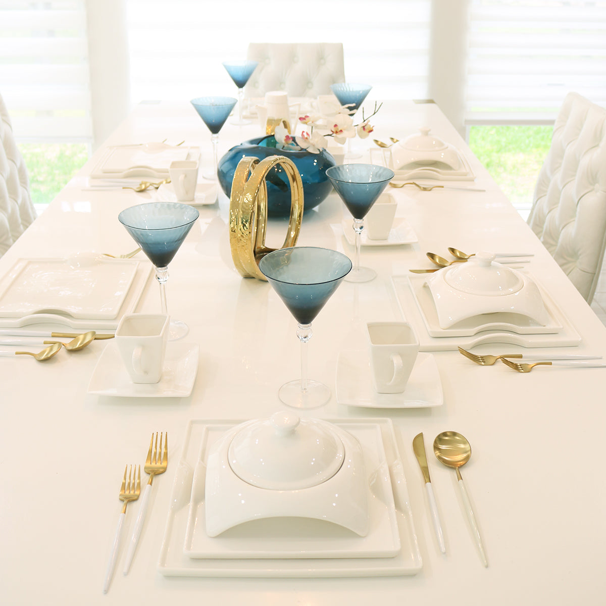 Elegant modern dining table with blue martini glasses, gold cutlery, and white dinnerware