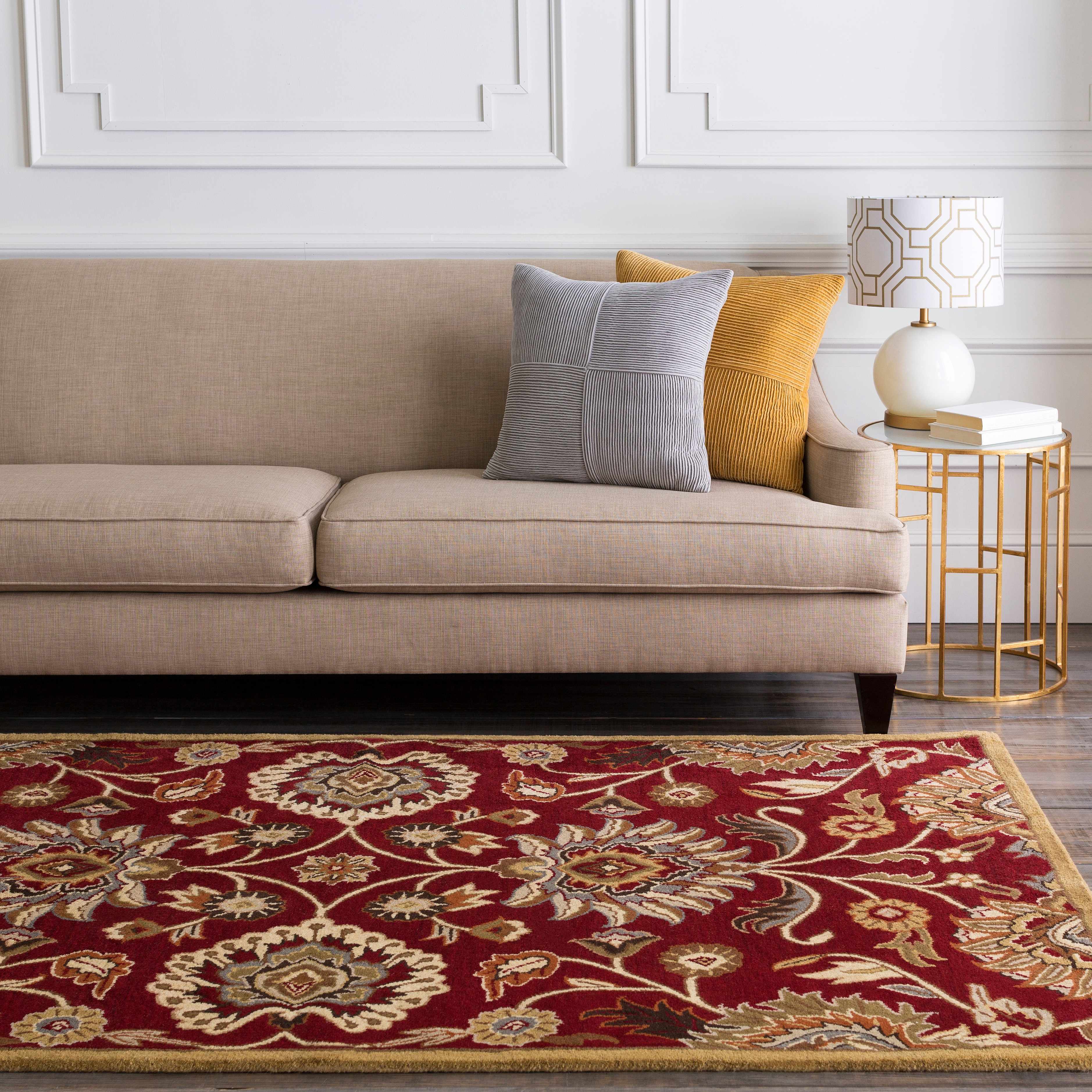 Beige sofa with decorative pillows on a red patterned rug in a living room setting.