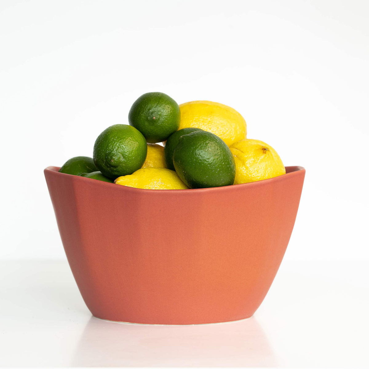 Bowl filled with lemons and limes on a white background