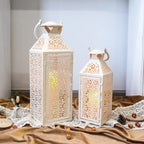 Two decorative lanterns on a table with a lace tablecloth and fruit.