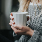 Person holding a white mug with steam, wearing a textured sweater.