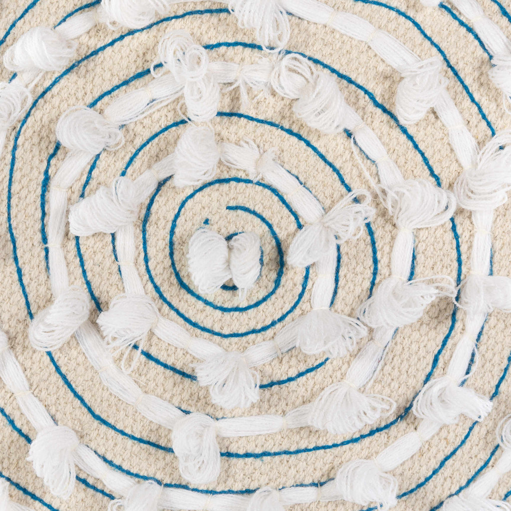 Close-up of a textured round ottoman top with blue concentric circles and tassels.