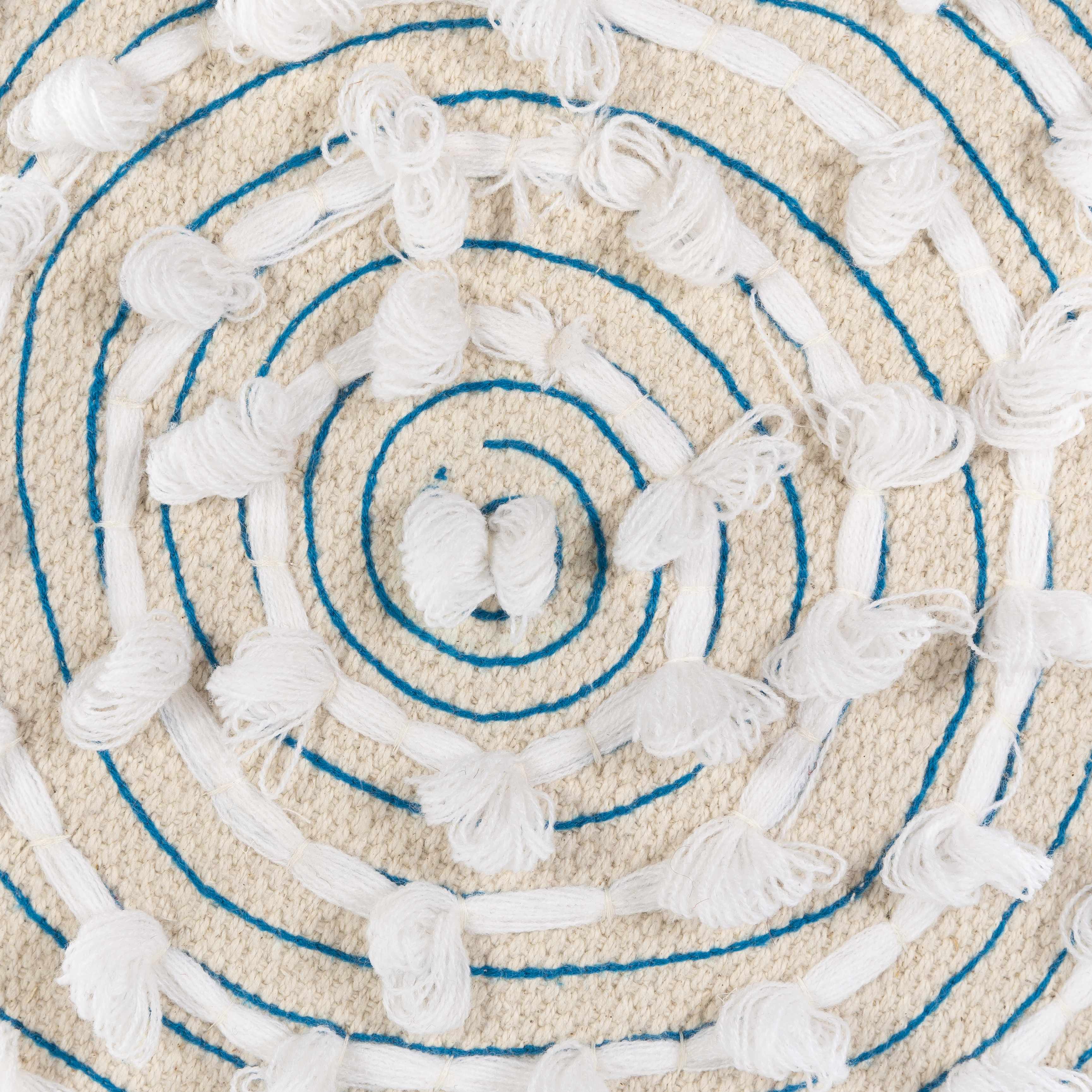 Close-up of a textured round ottoman top with blue concentric circles and tassels.